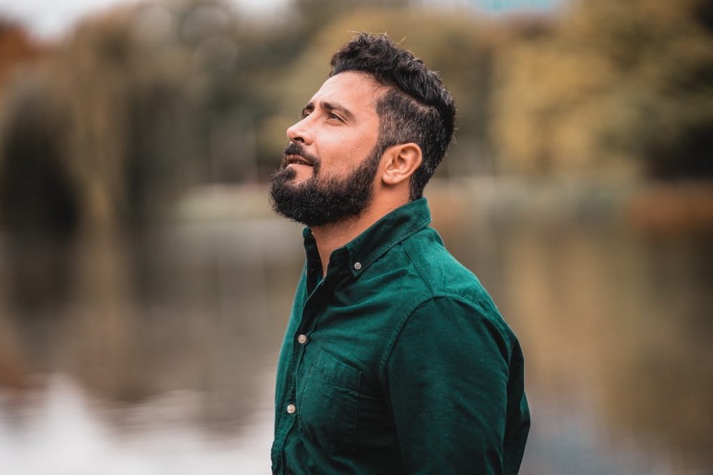 Man in green shirt looking upwards in front of a lake